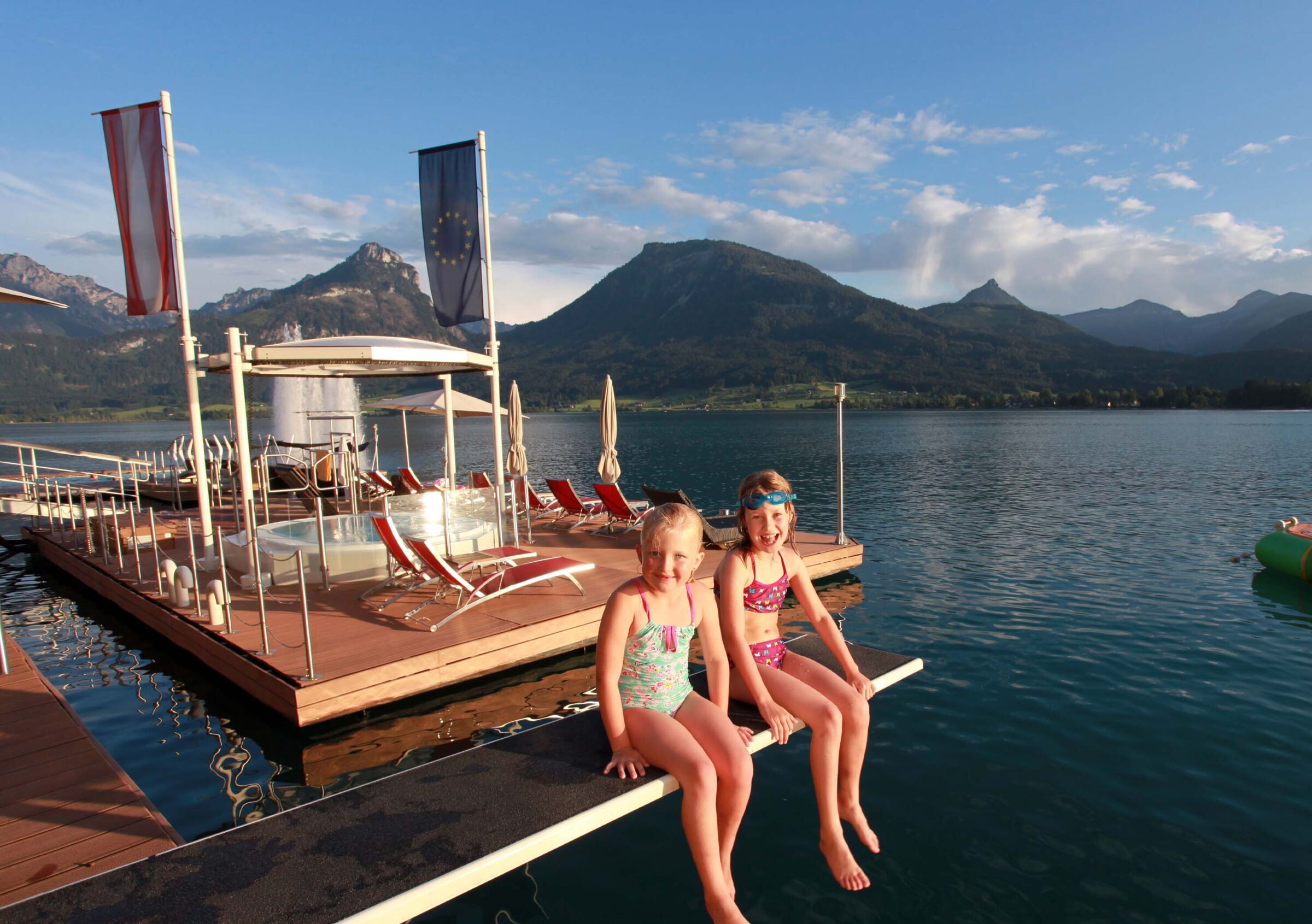 Zwei Mädchen sitzend auf einem Springbrett am Wolfgangsee vor dem Rösslpool des Hotels im Weissen Rössel