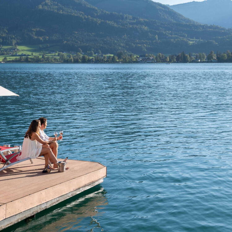 Pärchen mit einem Glas Sekt sitzend auf einer Sonnenliege im Weissen Rössl, eines der schönsten Wellnesshotels im Salzkammergut