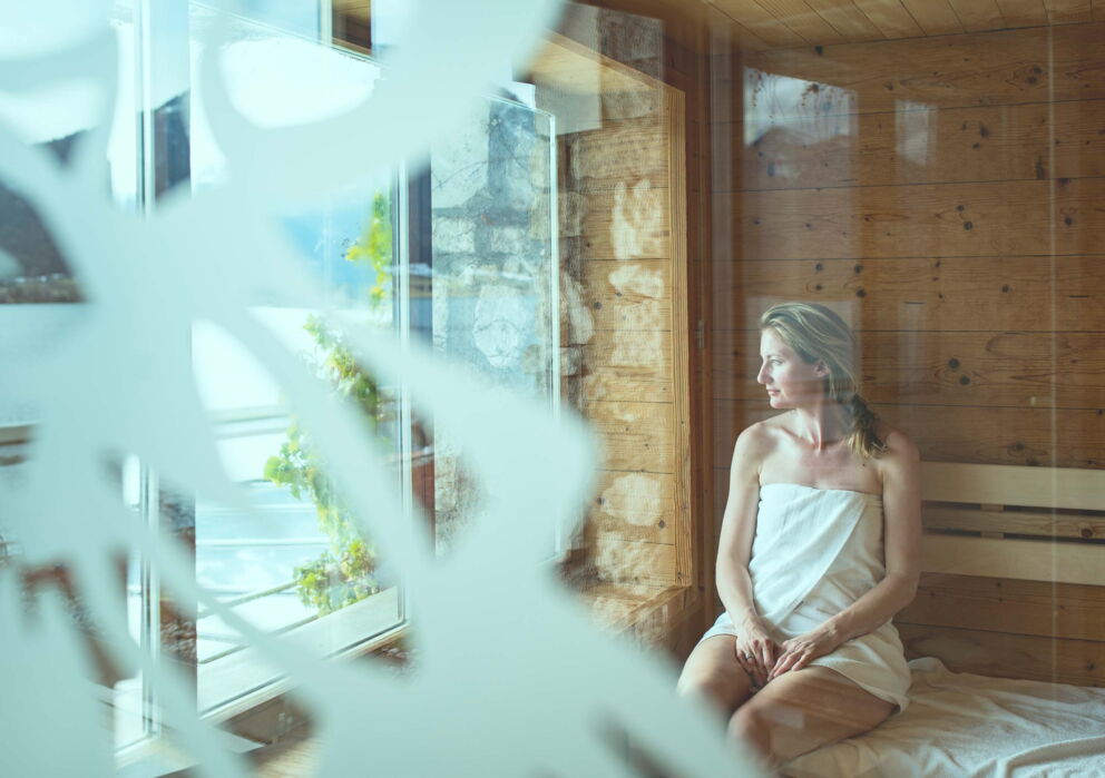 Frau in der Sauna im Weissen Rössl am Bestaunen der umliegenden Landschaft durch die Glasfassade