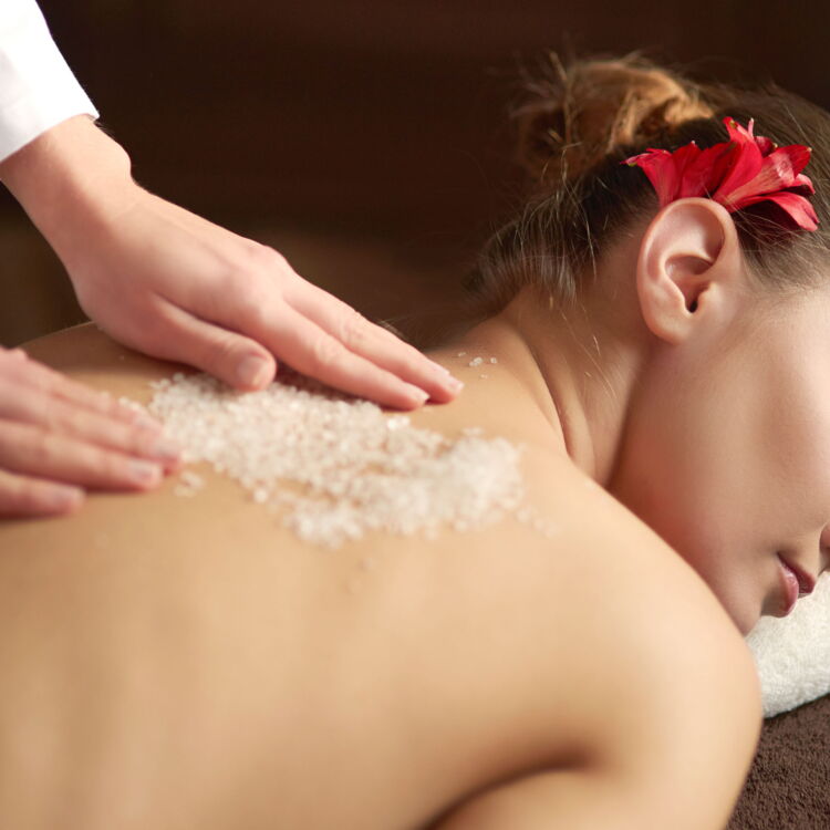 Frau bei einer Massage mit Salz am Rücken und einer Blume im Haar