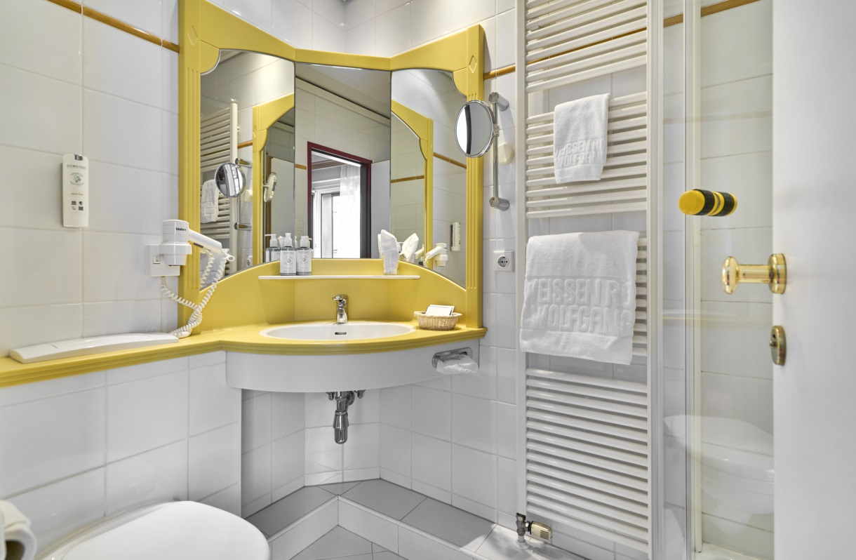 Bathroom at the Romantik Hotel Im Weissen Rössl on Lake Wolfgang, featuring a shower, toilet, sink, mirror, towel warmer, and light-colored tiles.