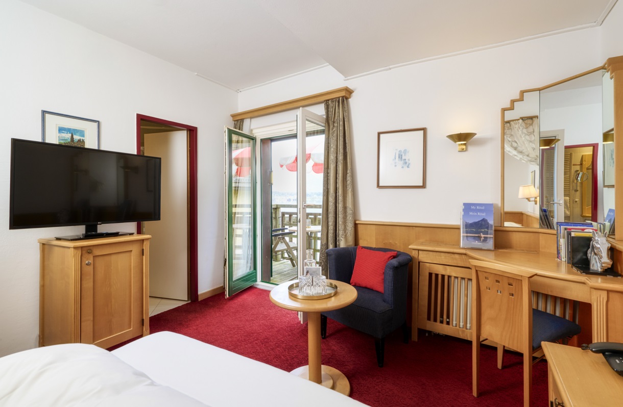 Rooms at the Romantik Hotel Im Weissen Rössl on Lake Wolfgang, featuring a bed, TV, desk, seating area, wooden furniture, and access to a balcony.