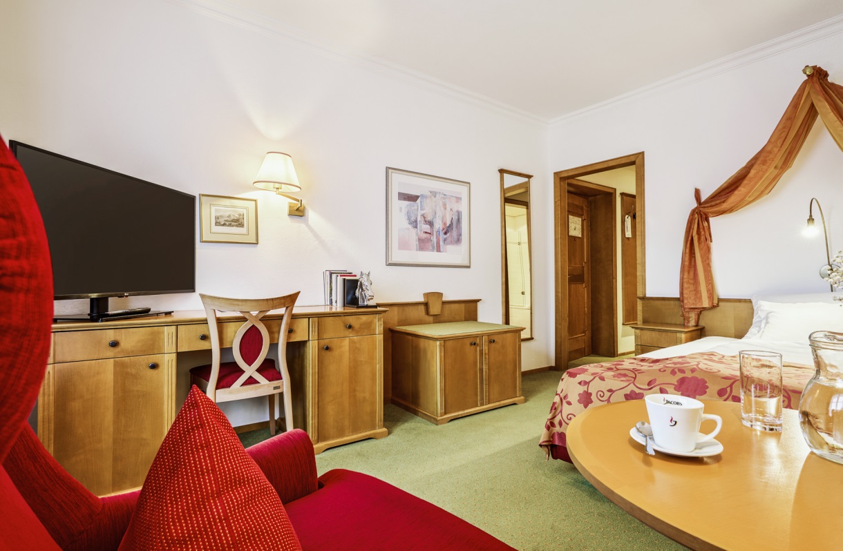 Single room at the Romantik Hotel Im Weissen Rössl on Lake Wolfgang, featuring a single bed, TV, desk, red armchair, small table, and classic wooden furnishings.