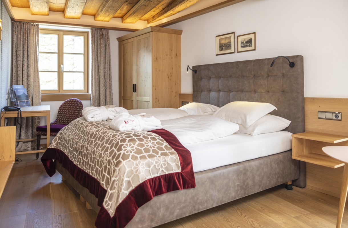 Doppelzimmer im Romantik Hotel Im Weissen Rössl am Wolfgangsee mit Doppelbett, Holzboden, Kleiderschrank, Schreibtisch, Sitzgelegenheit und sichtbaren Holzbalken an der Decke.