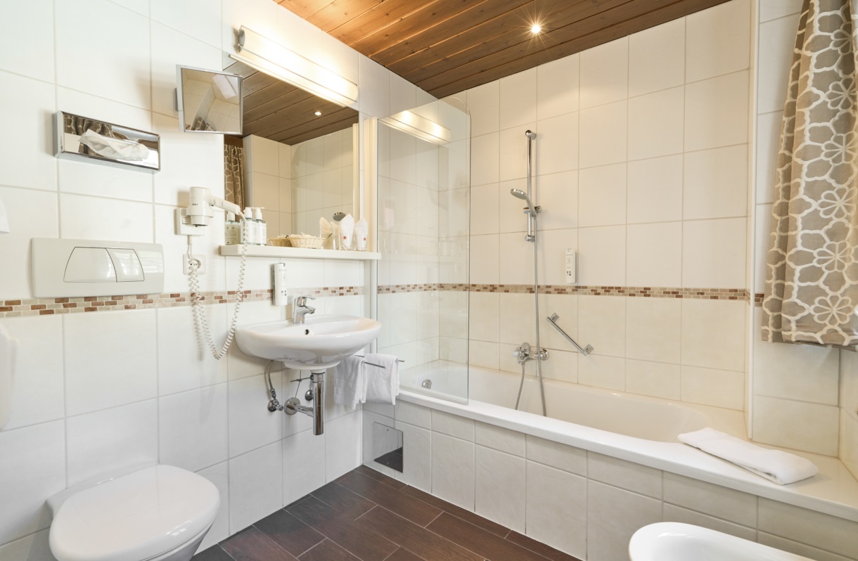 Badezimmer im Romantik Hotel Im Weissen Rössl am Wolfgangsee mit Badewanne, Duschvorrichtung, WC, Bidet, Waschtisch, Spiegel und hellen Fliesen.