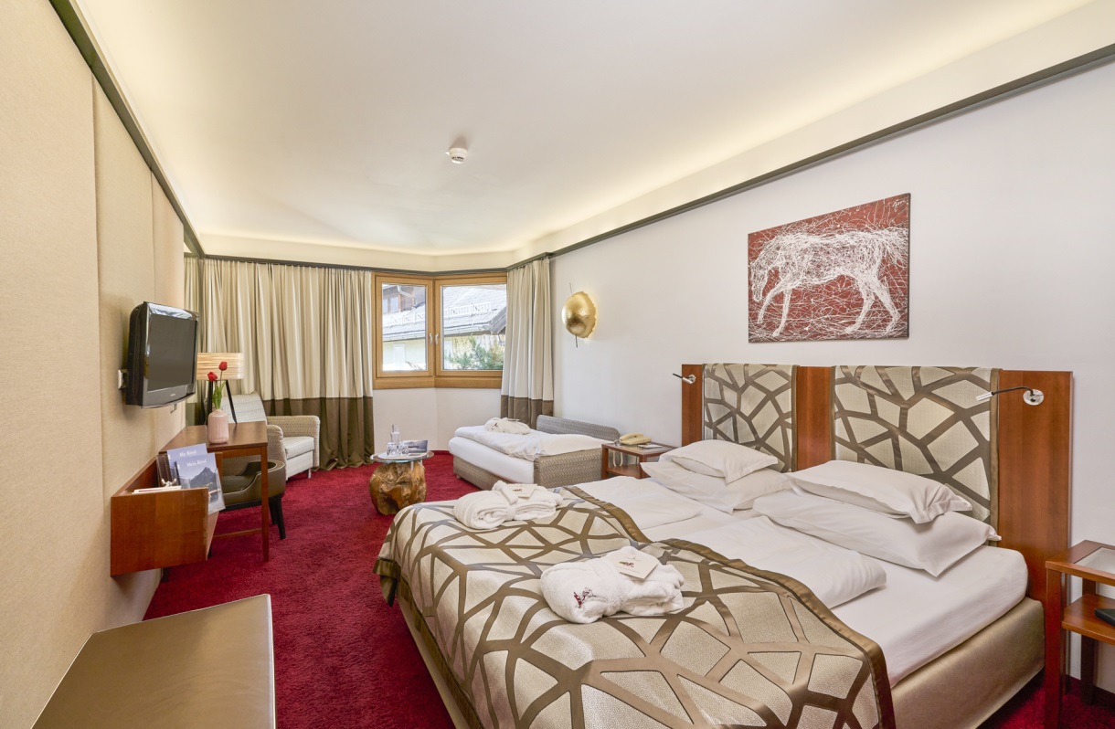 Doppelzimmer im Romantik Hotel Im Weissen Rössl am Wolfgangsee mit Doppelbett, zusätzlichem Einzelbett, Fernseher, Schreibtisch, Sitzbereich, Beistelltisch und Fensterfront.