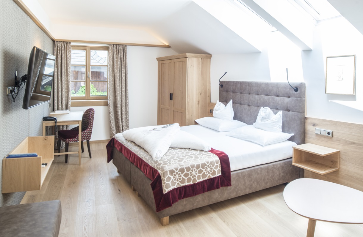 Doppelzimmer im Romantik Hotel Im Weissen Rössl am Wolfgangsee mit Doppelbett, Fernseher, Schreibtisch, Kleiderschrank, Holzboden, Dachfenstern und Sitzbereich.