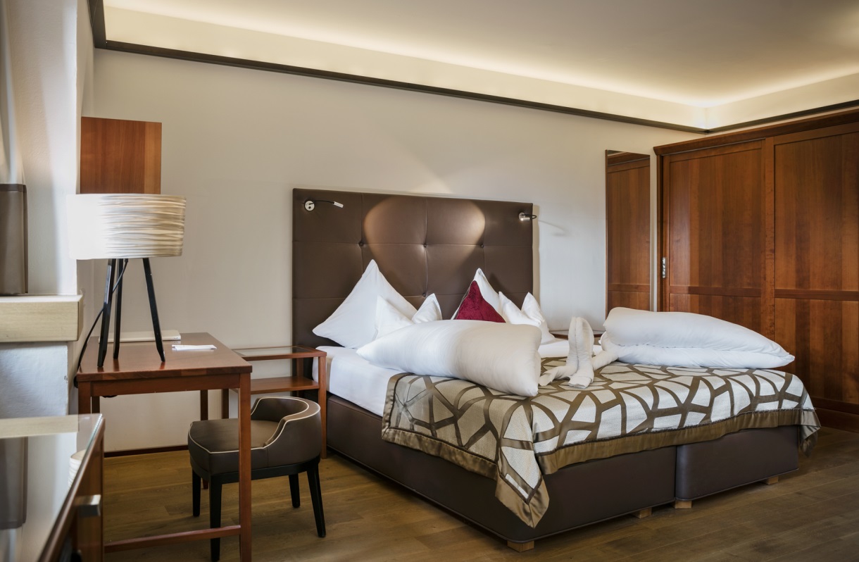 Doppelzimmer im Romantik Hotel Im Weissen Rössl am Wolfgangsee mit Doppelbett, Schreibtisch, Stuhl, Holzboden, großem Kleiderschrank und moderner Beleuchtung.