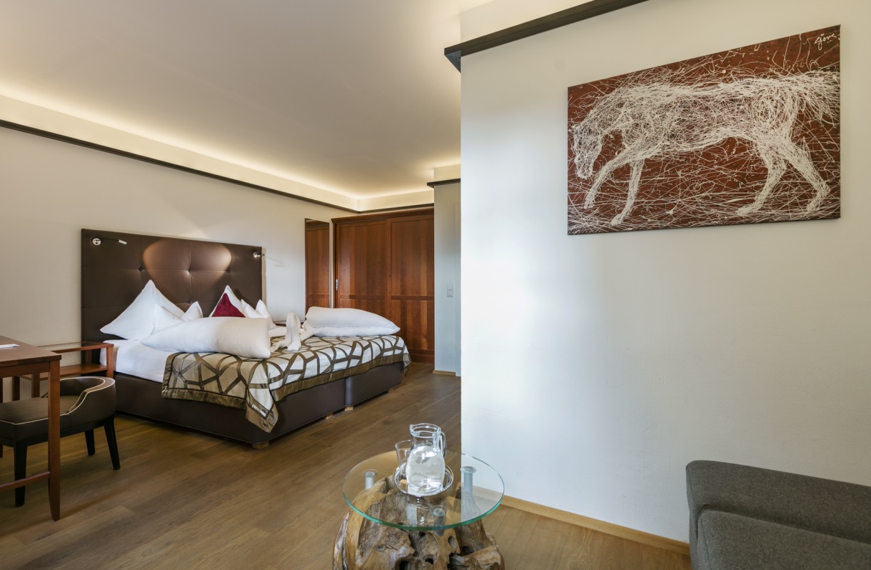 Doppelzimmer im Romantik Hotel Im Weissen Rössl am Wolfgangsee mit Doppelbett, Schreibtisch, Sitzbereich, Glastisch, Holzboden, Kleiderschrank und Wandbild.