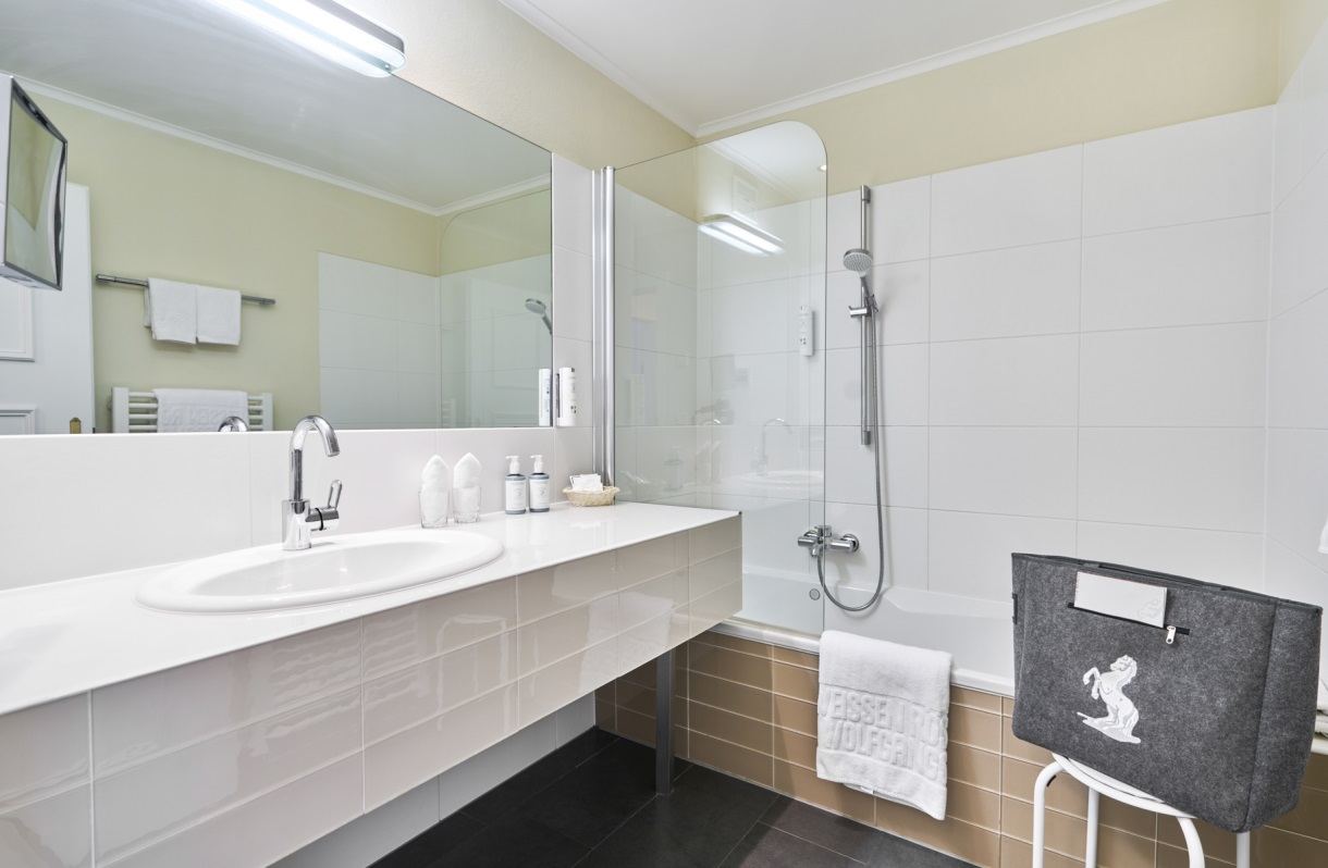 Bathroom at the Romantik Hotel Im Weissen Rössl on Lake Wolfgang, featuring a bathtub, shower, sink, large mirror, towel rack, and light-colored tilework.