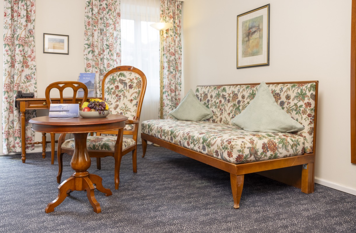 Seating area at the Romantik Hotel Im Weissen Rössl on Lake Wolfgang, featuring a patterned sofa, armchairs, a round table, floral curtains, and classic furnishings.