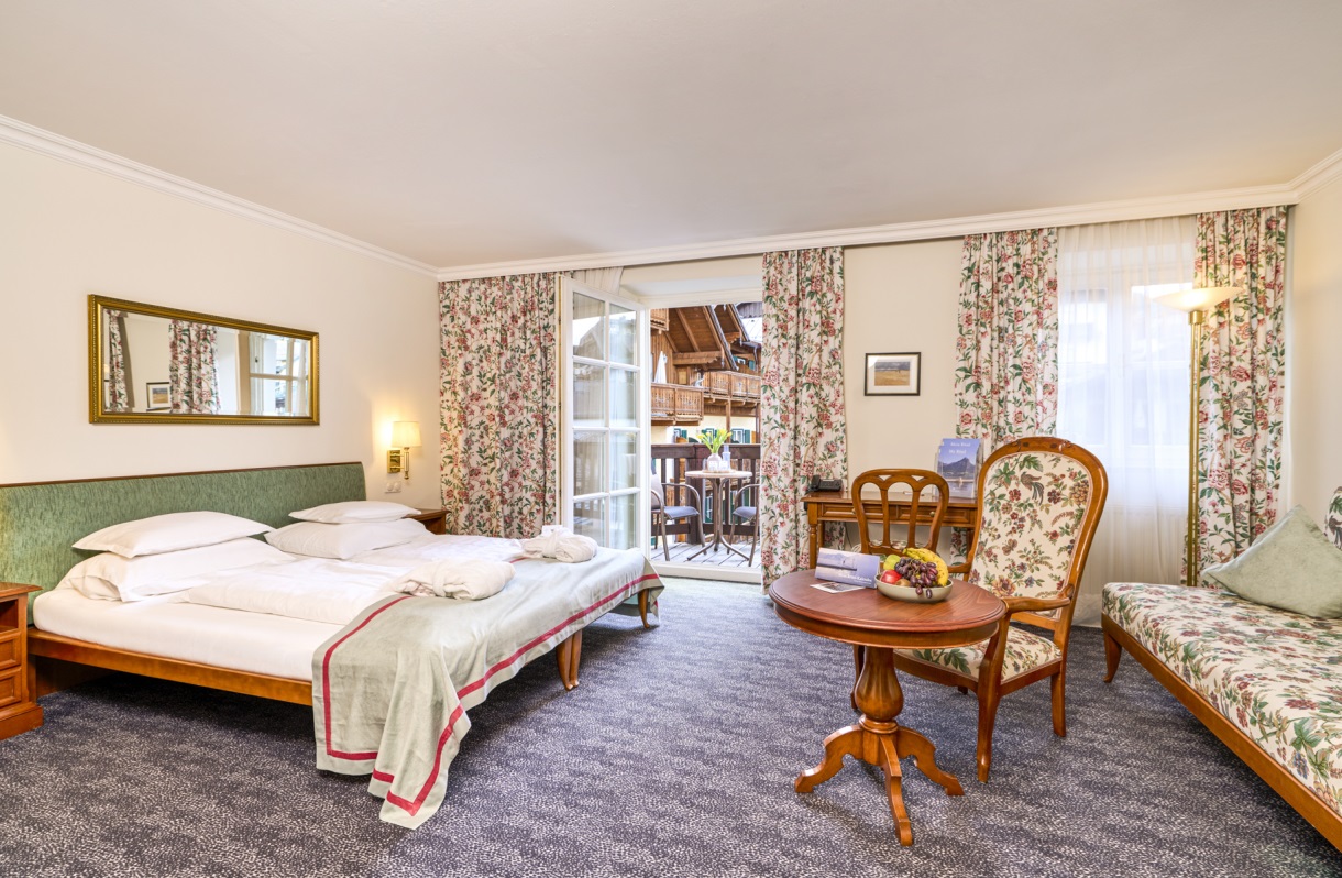 Double room at the Romantik Hotel Im Weissen Rössl on Lake Wolfgang, featuring a double bed, sofa, armchairs, a round table, classic furnishings, and access to a balcony.