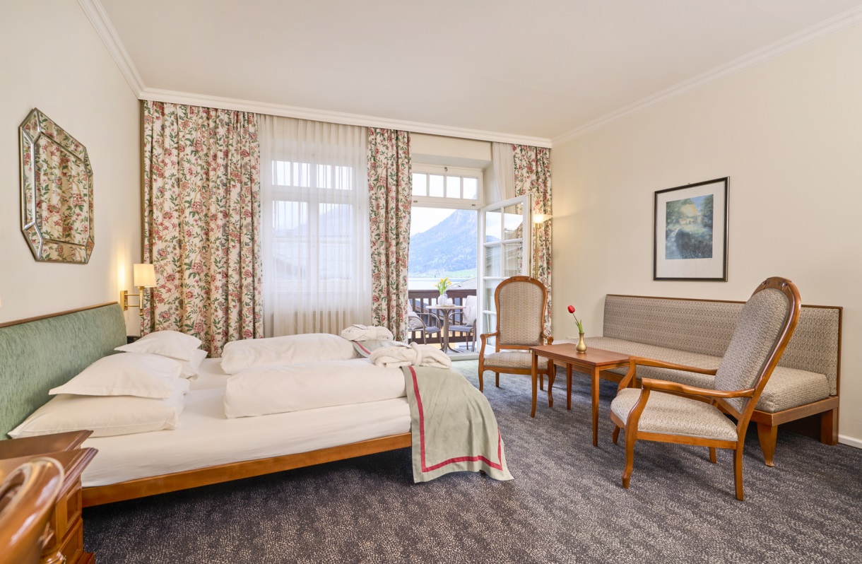 Double room at the Romantik Hotel Im Weissen Rössl on Lake Wolfgang, featuring a double bed, a sitting area, armchairs, a small table, classic furnishings, and a balcony overlooking Lake Wolfgang.