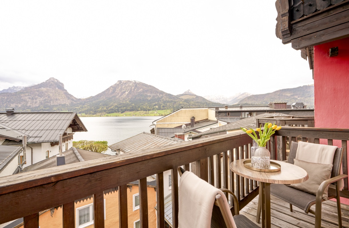 Balkon im Romantik Hotel Im Weissen Rössl am Wolfgangsee mit zwei Sesseln, kleinem Tisch, Holzgeländer und Blick auf den Wolfgangsee sowie die umliegende Berglandschaft.