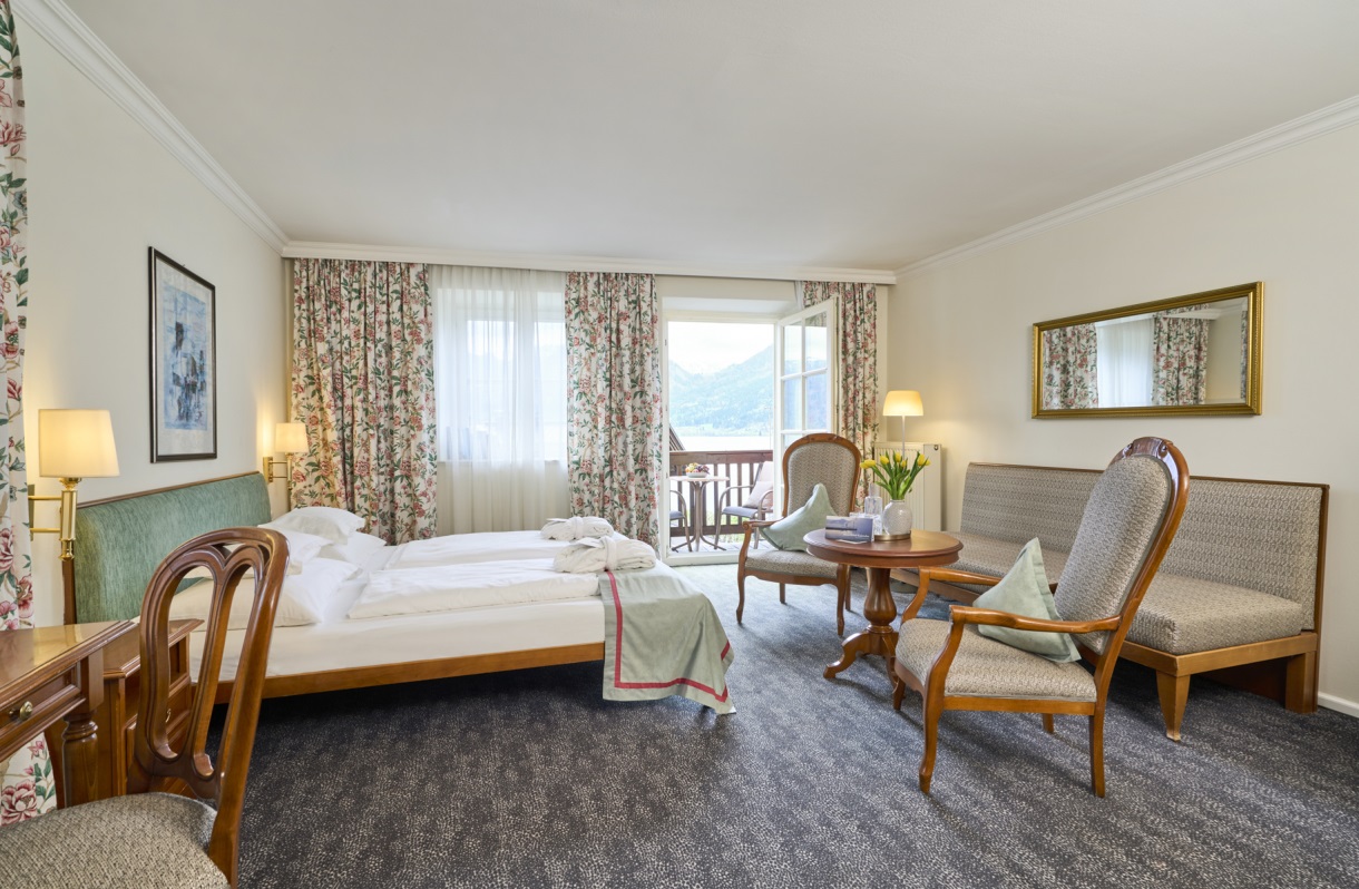 Doppelzimmer im Romantik Hotel Im Weissen Rössl am Wolfgangsee mit Doppelbett, Schreibtisch, Sitzbereich, Sofa, Sesseln, rundem Tisch, klassischer Einrichtung und Balkonzugang mit Blick auf den Wolfgangsee.