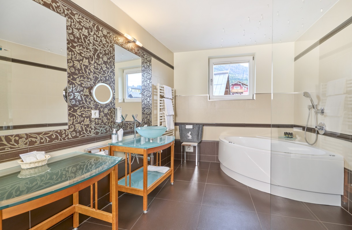 Badezimmer im Romantik Hotel Im Weissen Rössl am Wolfgangsee mit Whirlpool Badewanne, Duschbereich, Waschtisch, Spiegel, Handtuchheizkörper und großzügiger Ausstattung.