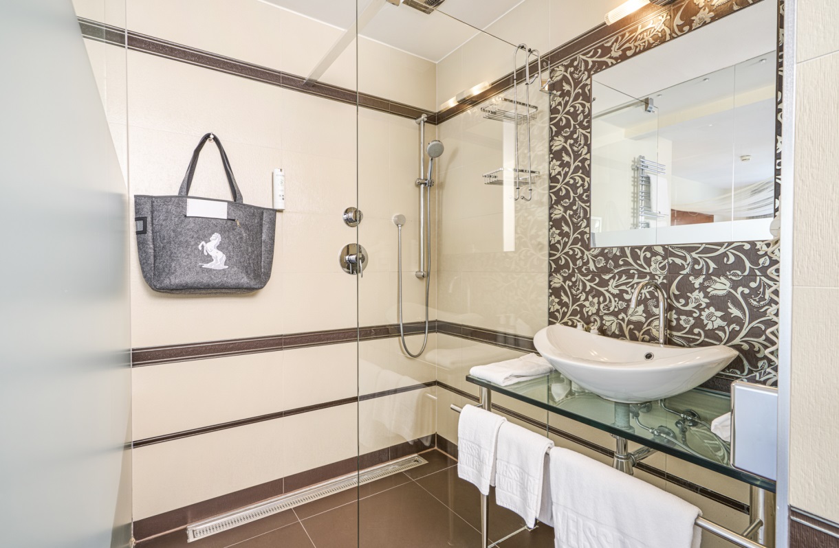Badezimmer im Romantik Hotel Im Weissen Rössl am Wolfgangsee mit Dusche, Glasabtrennung, Waschtisch, Spiegel, Handtuchablage und moderner Fliesenausstattung.