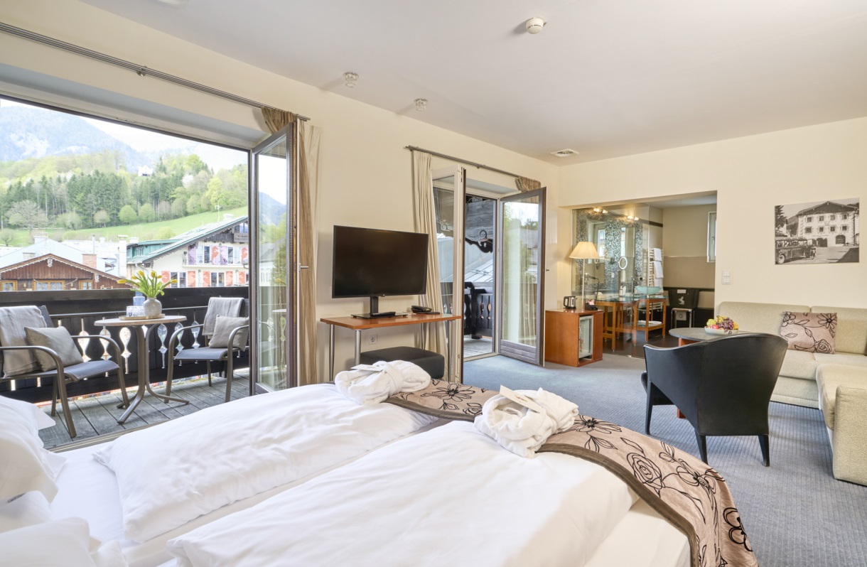 Großzügiges Zimmer im Romantik Hotel Im Weissen Rössl am Wolfgangsee mit Doppelbett, Fernseher, Sitzbereich, Sofa, Sessel und Balkonzugang mit Blick auf die Umgebung.