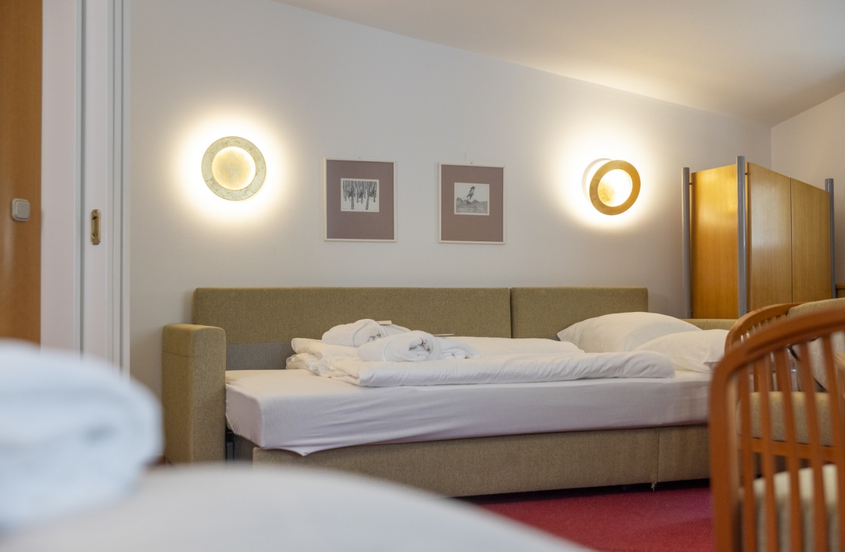 Schlafbereich im Familienzimmer des Romantik Hotel Im Weissen Rössl am Wolfgangsee mit Schlafsofa, Kleiderschrank, Wandbeleuchtung, Bildern und klassischer Einrichtung.